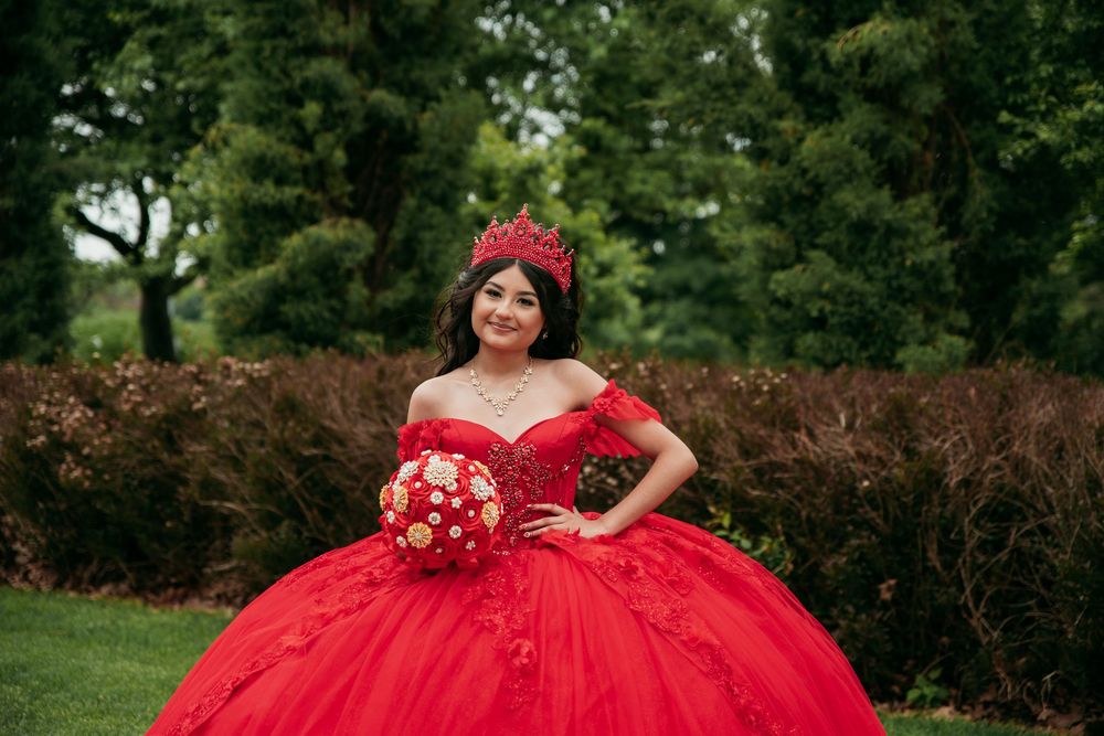 Vibrant red quinceañera dress photographed in a lush garden setting.