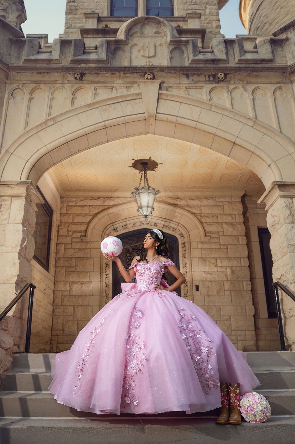 A person in a voluminous pink quinceañera gown with floral details poses under an ornate stone archway entrance.