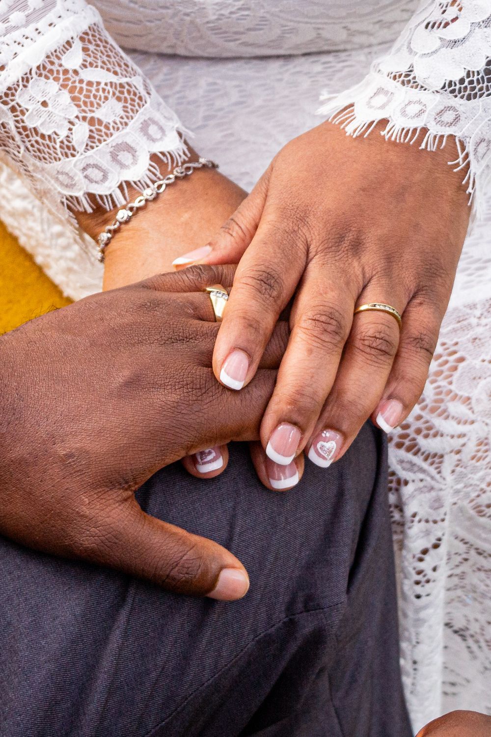Close-up view of French manicured nails on dark fabric against white lace background.