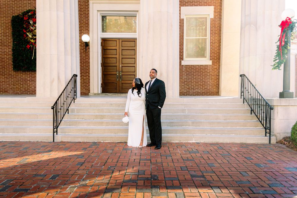 Newlyweds walk hand in hand along a brick path outside a traditional colonial-style church building.