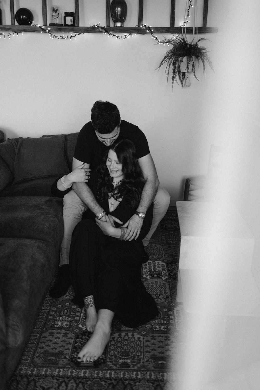 A black and white intimate moment shared on a couch with a hanging plant and decorative wall accents visible.
