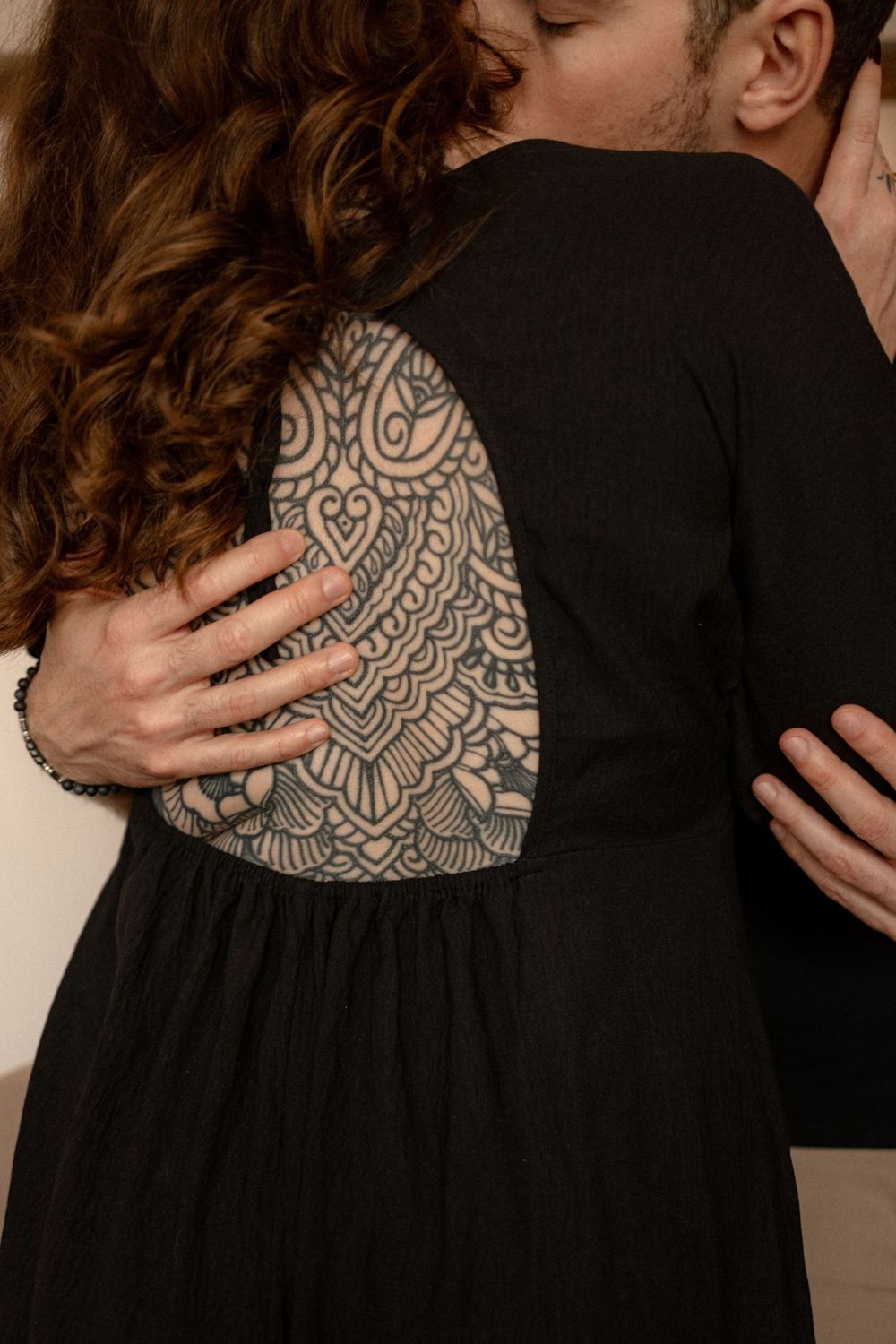 Close-up details of couple embracing, showing intricate tattoo patterns against black dress.
