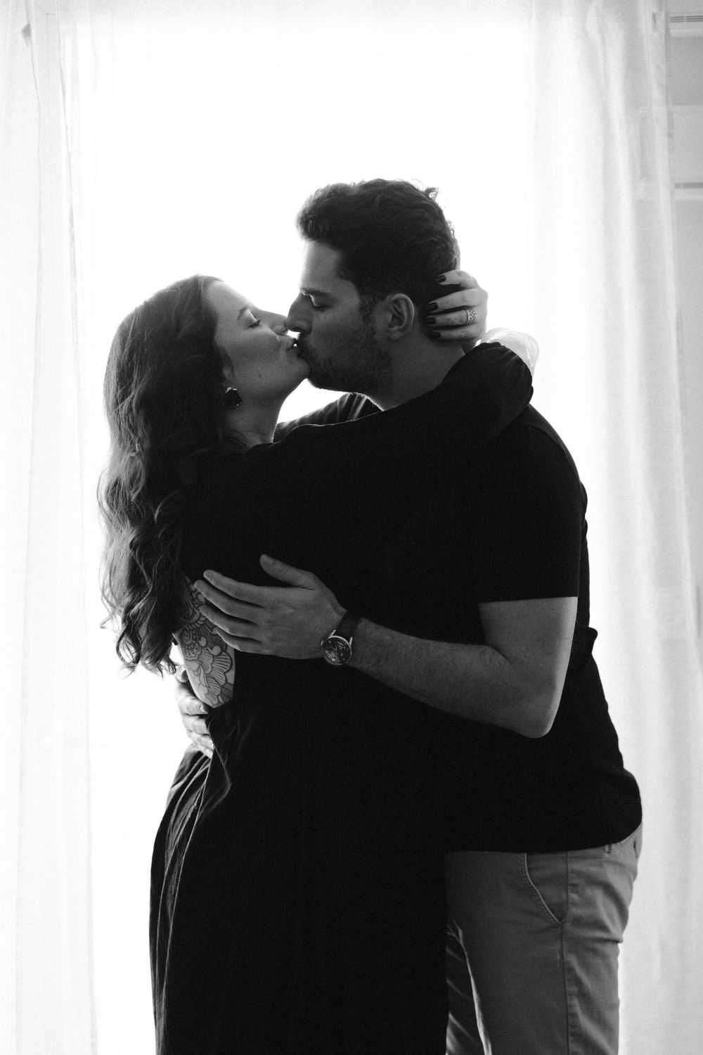 Romantic black and white photo series showing intimate couple embracing in soft window light.