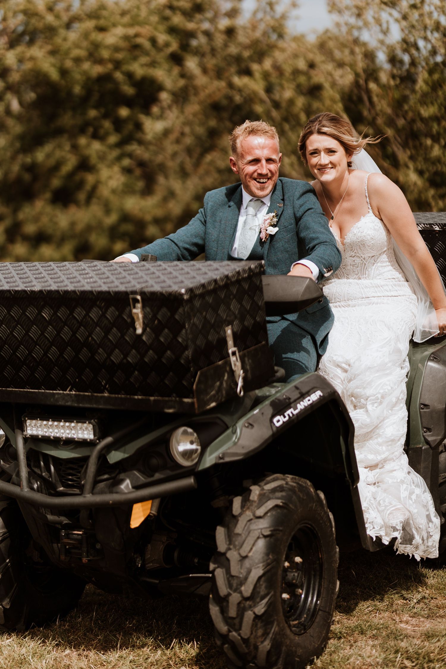 A couple in wedding attire poses together on a black quadbike.