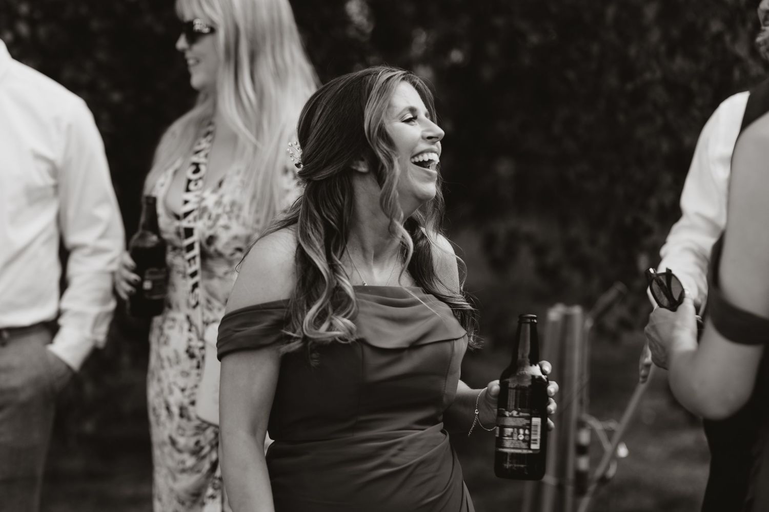 A candid black and white photo of a guest laughing joyfully at an outdoor party with a drink in hand.