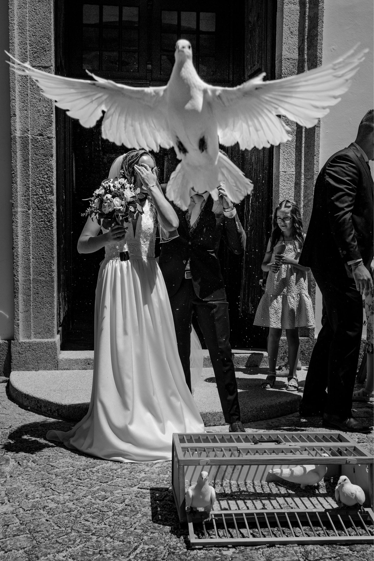 A white dove spreads its wings in front of a wedding party outside a building entrance.