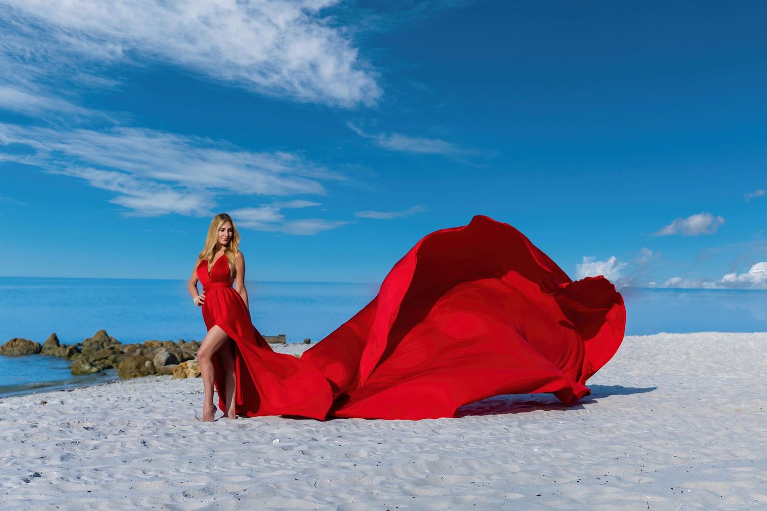 A person in a flowing red dress stands on a white salt flat against a vivid blue sky. Flying Dress Photoshoot