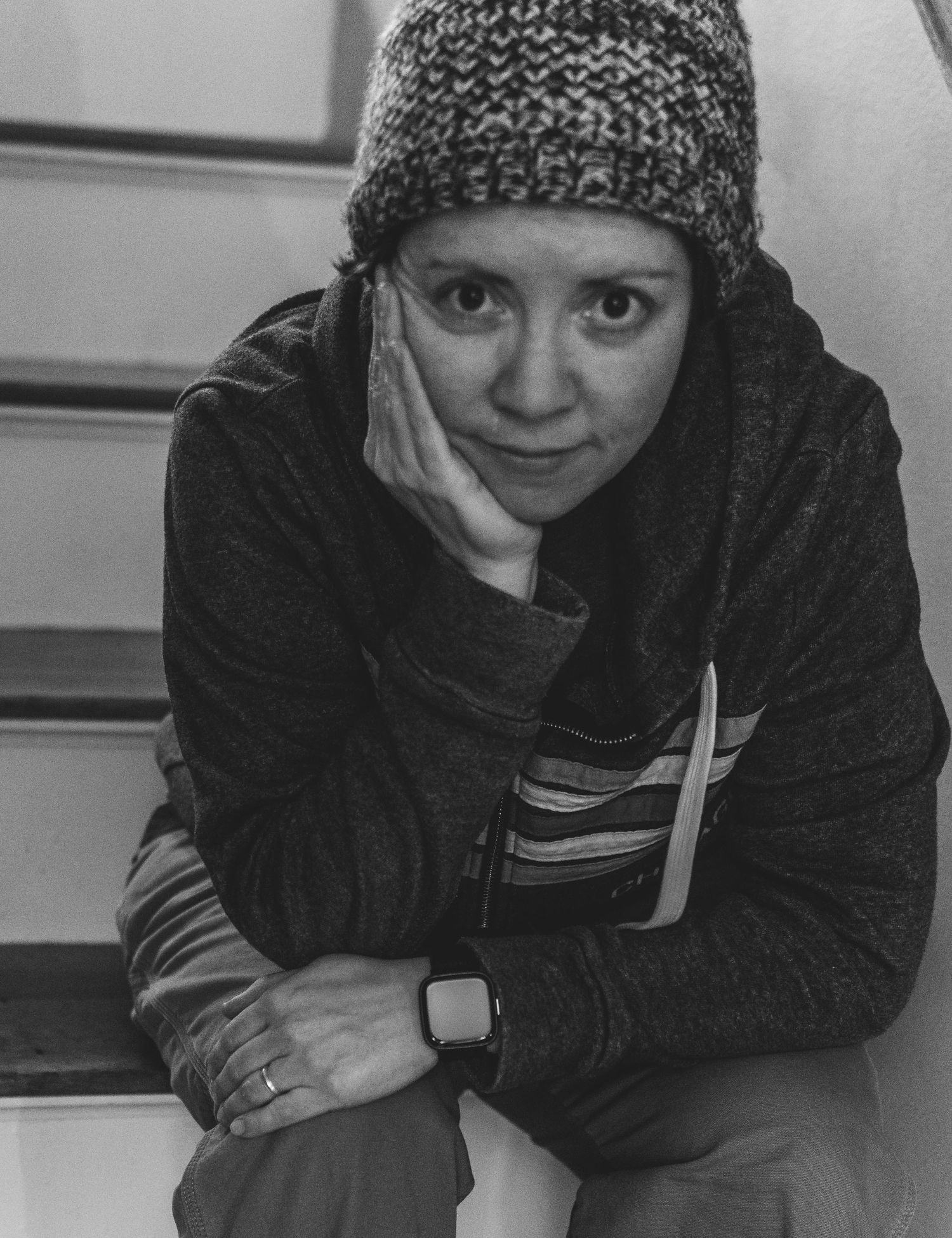 Black and white portrait of someone wearing a knit winter hat and dark jacket while resting their chin on their hand.