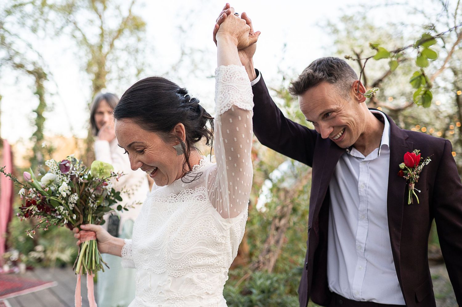 Bride leads groom along a path, holding hands in the air, both smiling