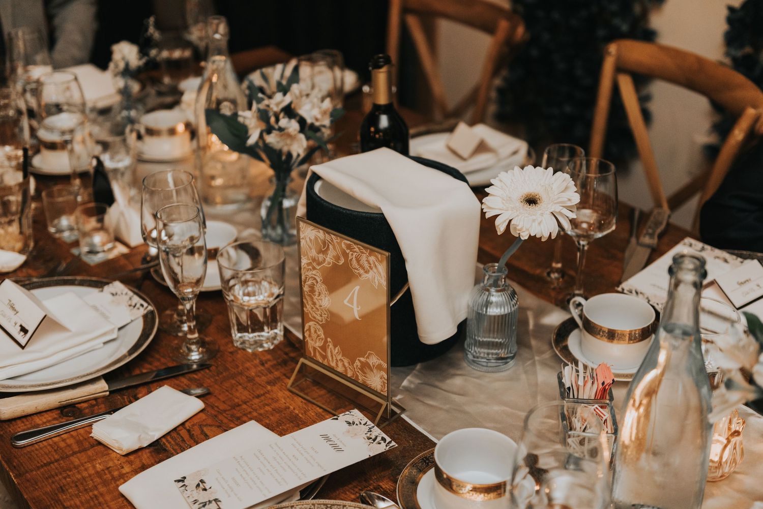 Rustic wedding reception table setting with glowing lanterns, white linens, and elegant glassware on wooden tables.