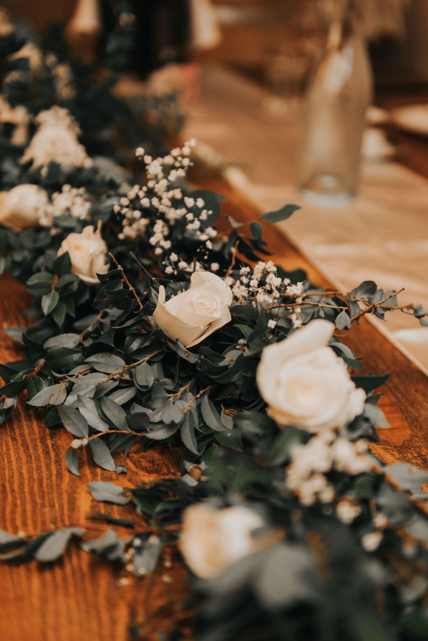 Wedding decor detail showing delicate white flowers and eucalyptus greenery arranged on a rustic wooden surface.