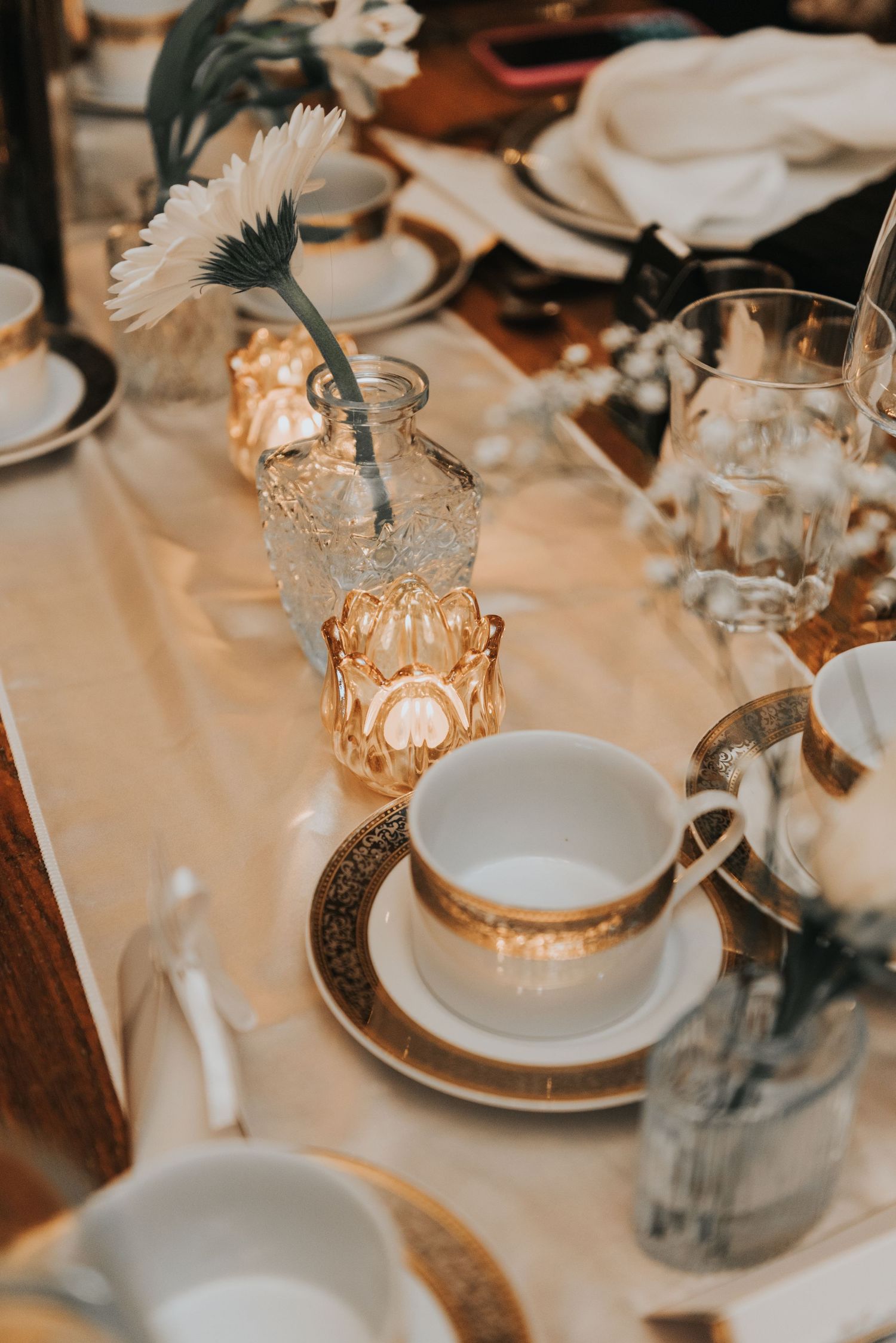 Elegant table setting with warm glowing candle holders, white plates, and delicate floral arrangements at a formal dinner.