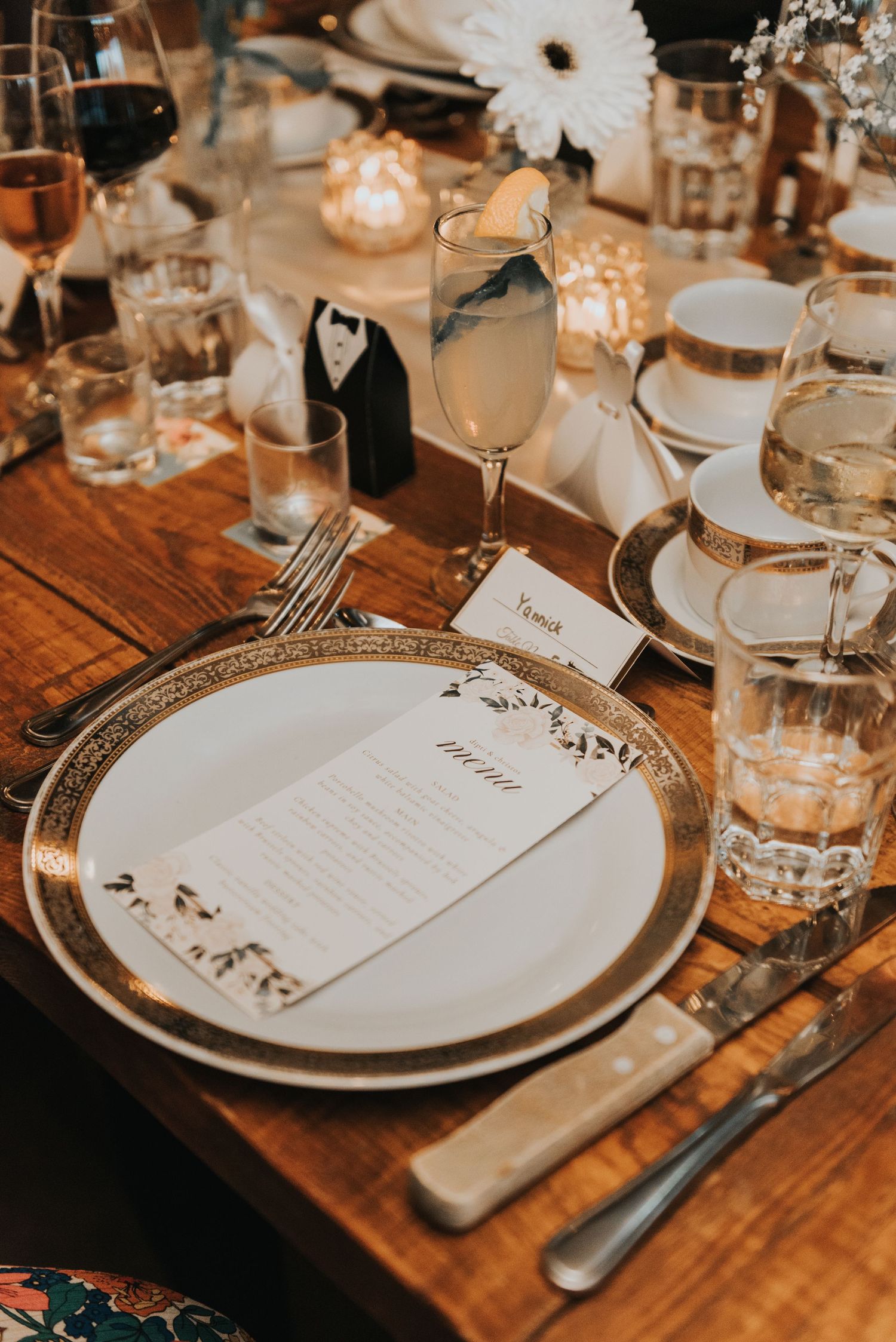 Elegant place settings at a wedding reception with white plates and menus on rustic wooden tables in warm lighting.
