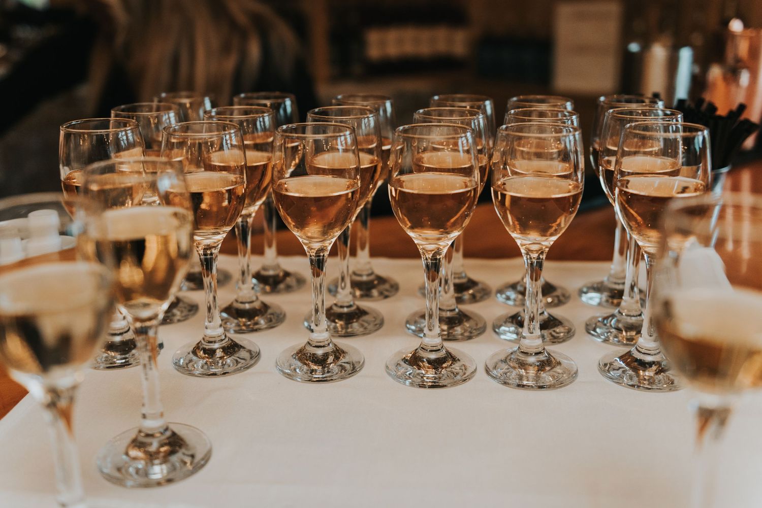 Empty wine glasses lined up on a wooden table at a restaurant or event venue in warm lighting.