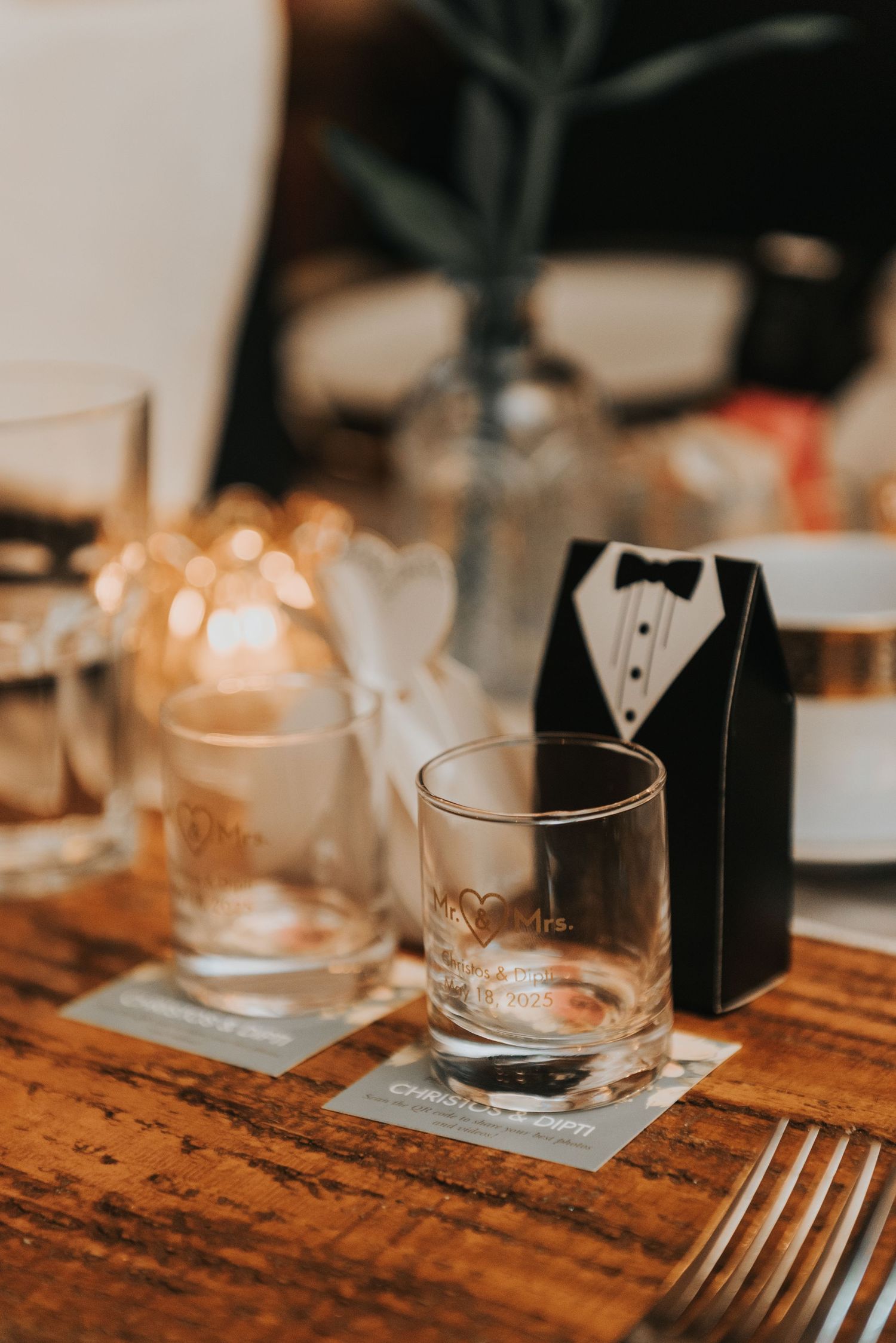 Wedding table place settings with tuxedo-styled decorations and glassware on a rustic wooden surface.