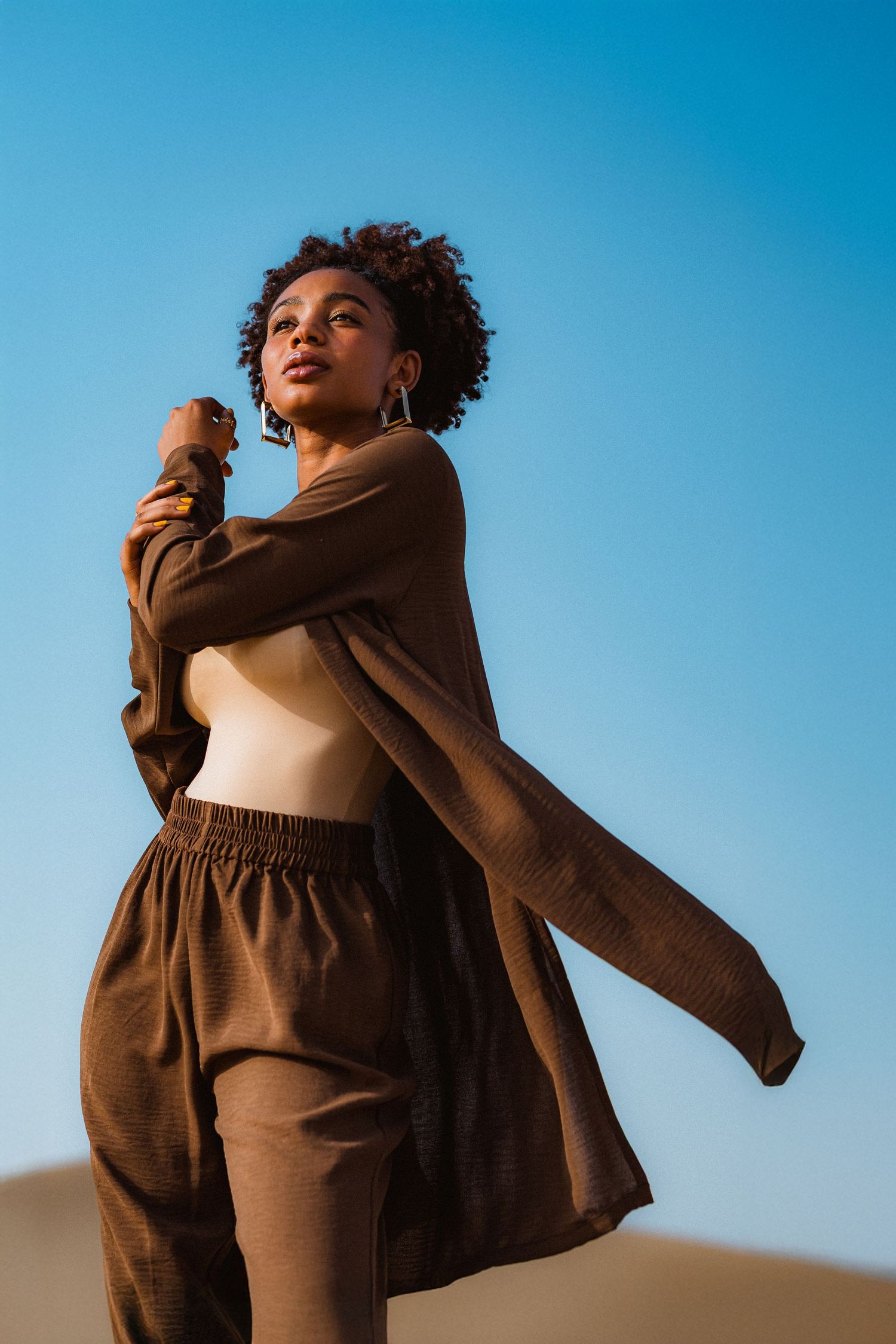Editorial fashion portrait in Dubai desert featuring model in flowing brown outfit