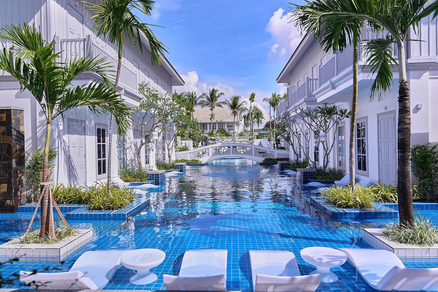 Luxurious beachfront resort with white buildings, palm trees and multiple swimming pools along a tropical coastline.