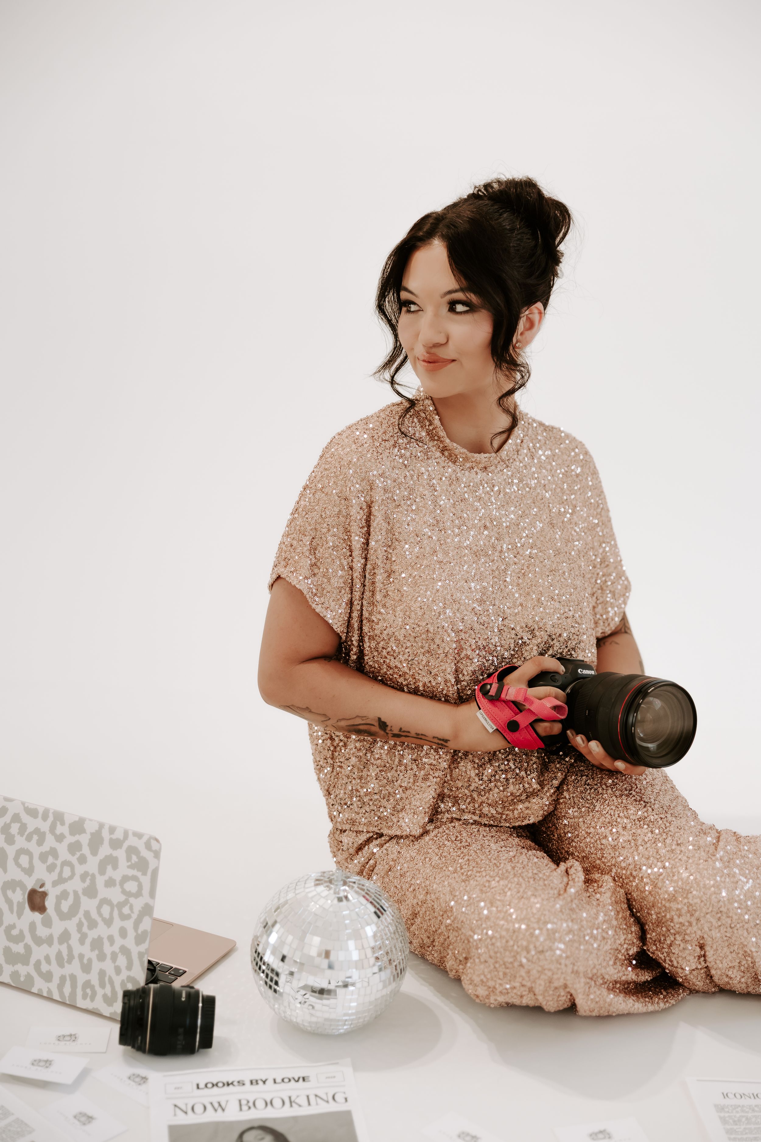 Someone in a sparkly rose gold dress sits with boxing gloves in a minimalist white setting.