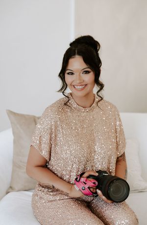 A person in a sequined champagne dress poses with pink boxing gloves on a white couch.