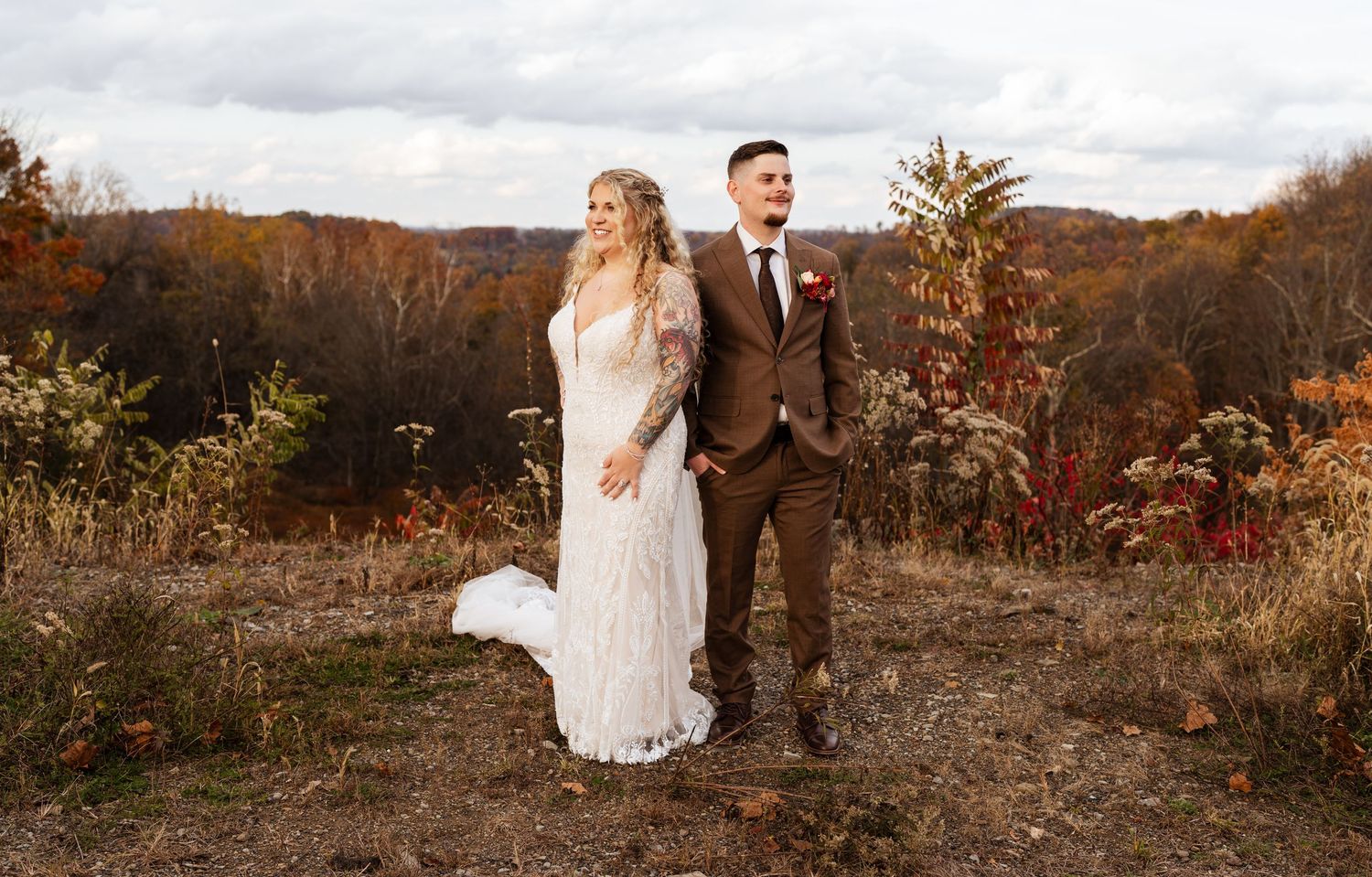 A couple stands together on a hilltop surrounded by autumn foliage during a fall wedding photoshoot.
