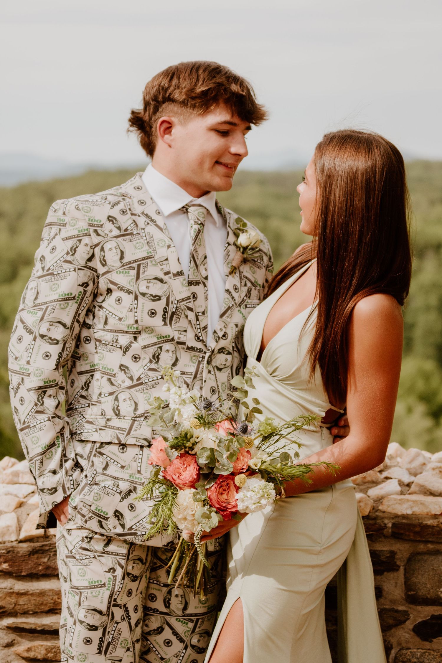 A wedding party in blue and white dresses stands against a rustic stone wall during a celebration.