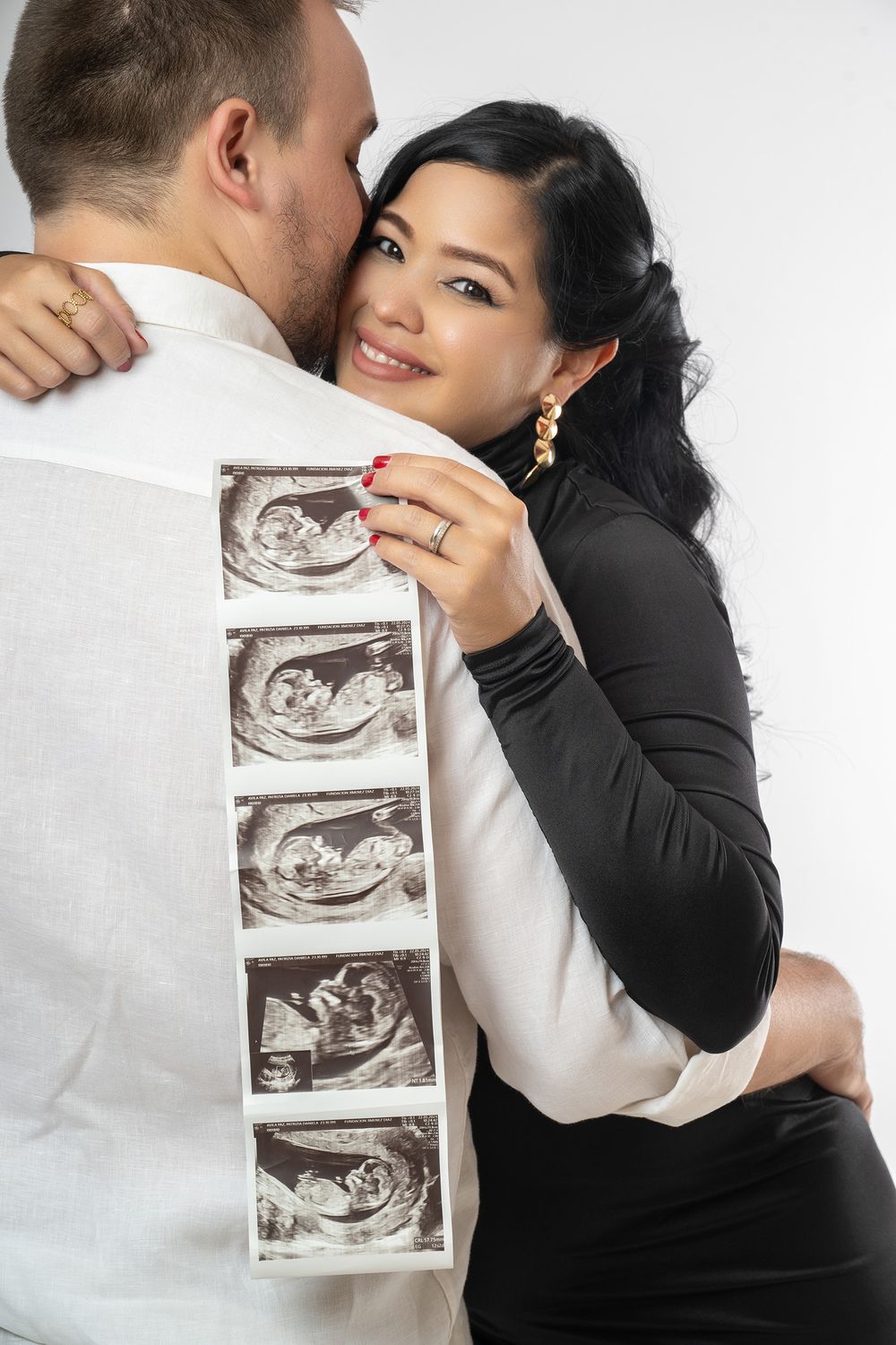 A couple embraces while holding ultrasound photos in a romantic pregnancy announcement photoshoot.