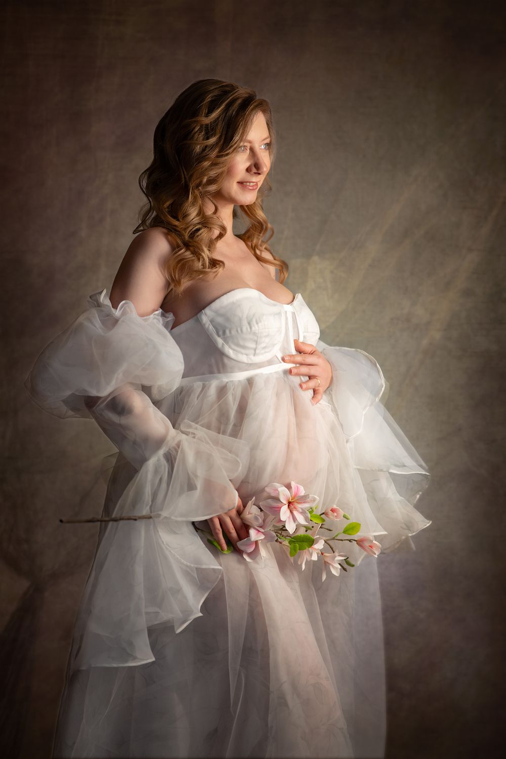 Ethereal portrait featuring flowing white tulle dress with delicate pink flowers against a moody dark backdrop.