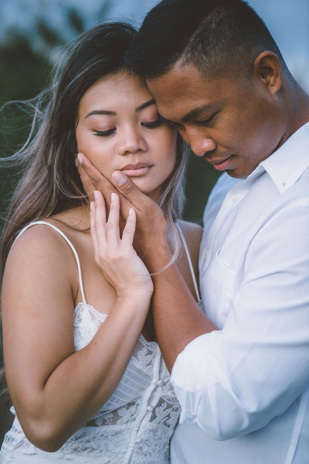 Intimate close-up portrait of couple sharing tender moment against natural backdrop.