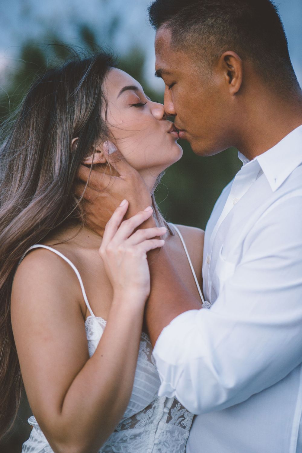 Romantic couple in white clothing shares intimate moments during outdoor photoshoot.
