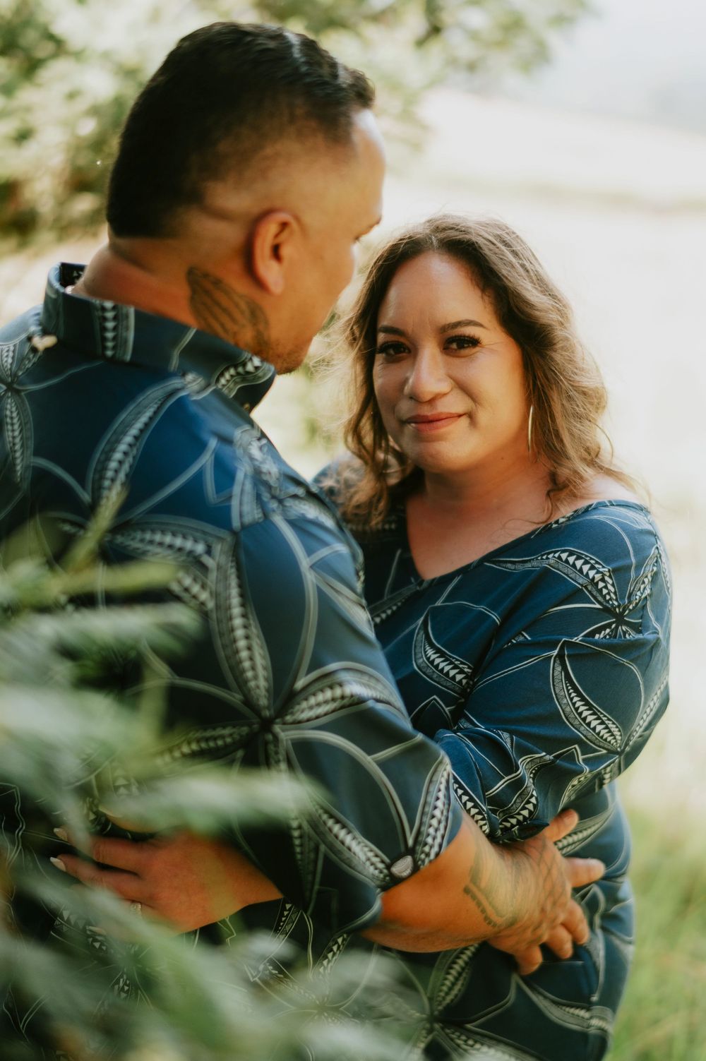 A couple in matching blue patterned outfits share an intimate moment outdoors.