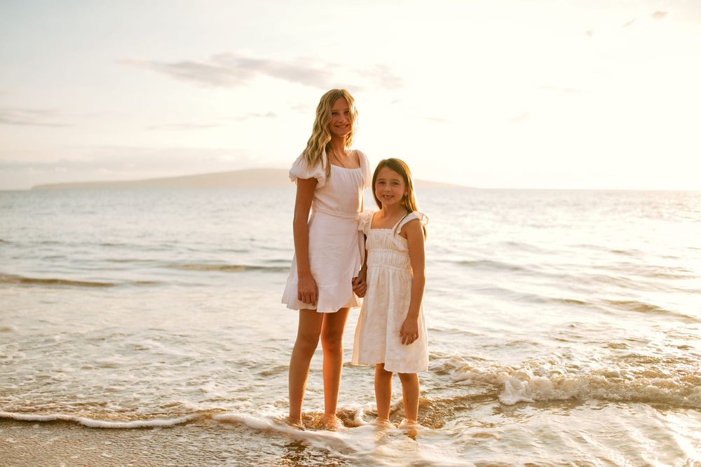 Family enjoying a sunset beach photoshoot together in white outfits along the shoreline.