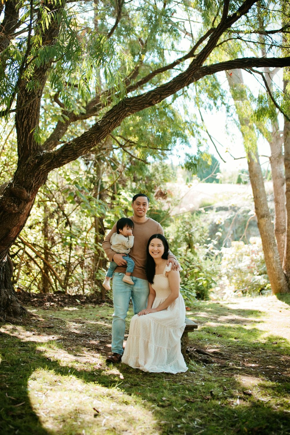A family poses together under a large tree with dappled sunlight filtering through the branches.