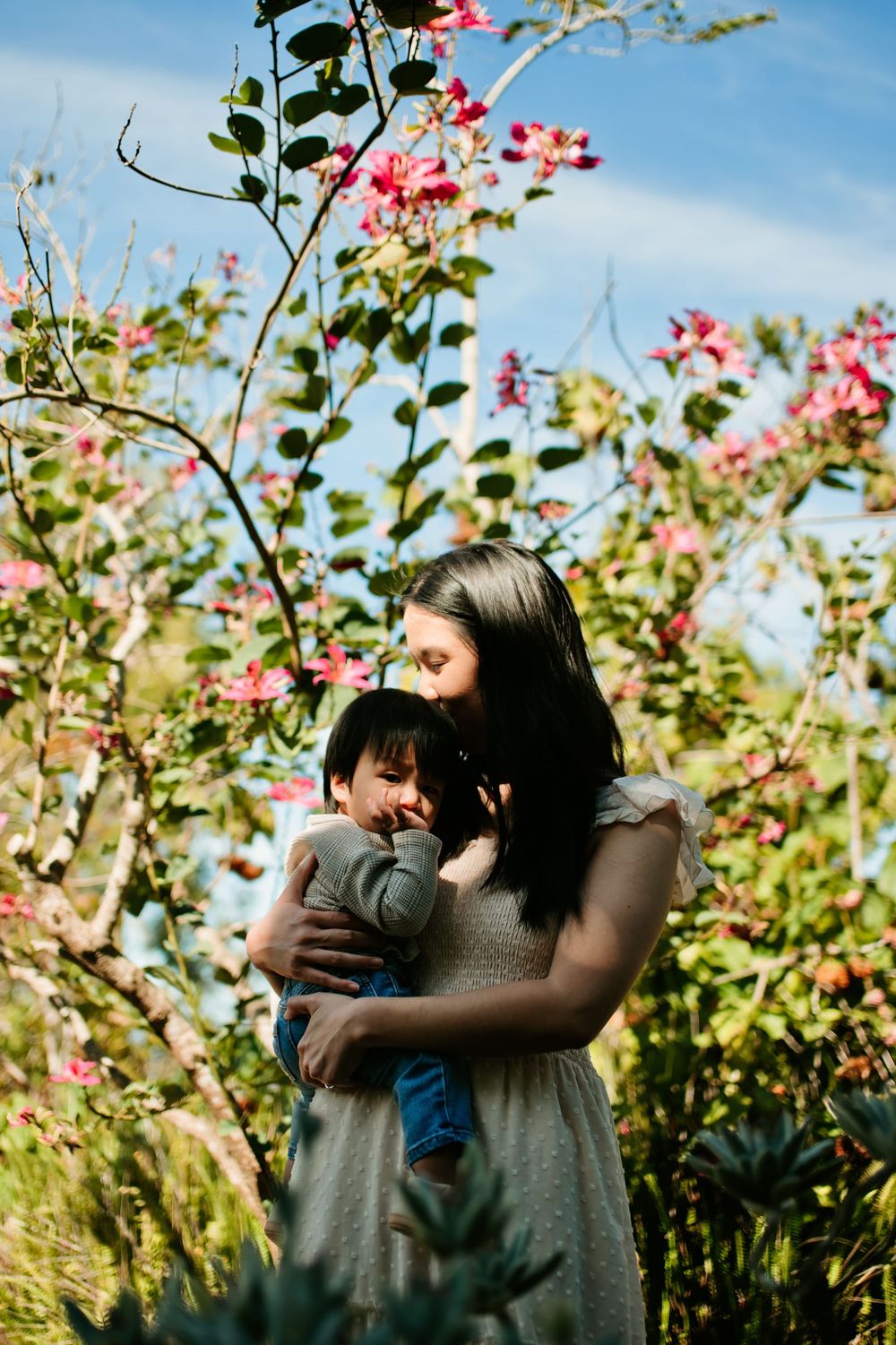 A tender moment captured in a garden with pink flowers blooming against a blue sky.