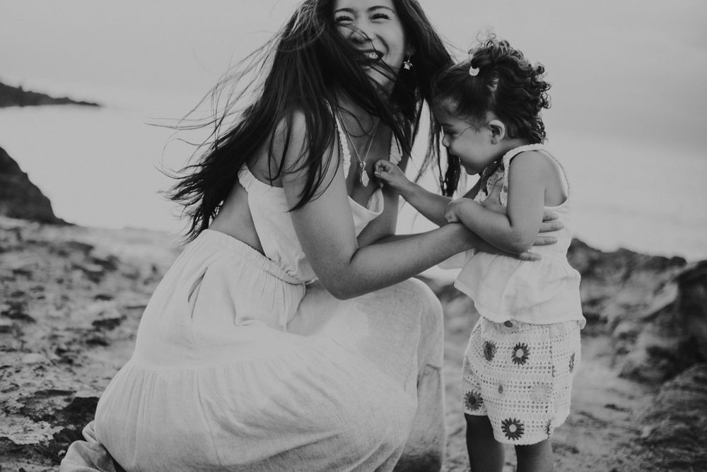 A joyful candid black and white photo of parent and child laughing together on a beach.