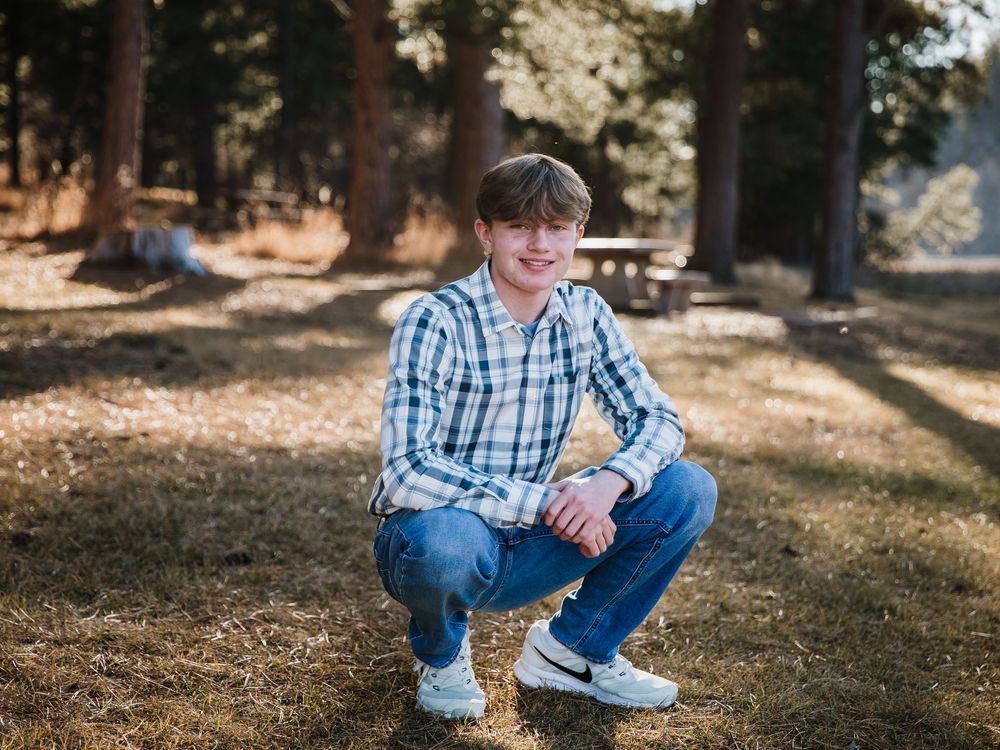 Person in casual attire sitting on grass near tree trunk in outdoor setting.