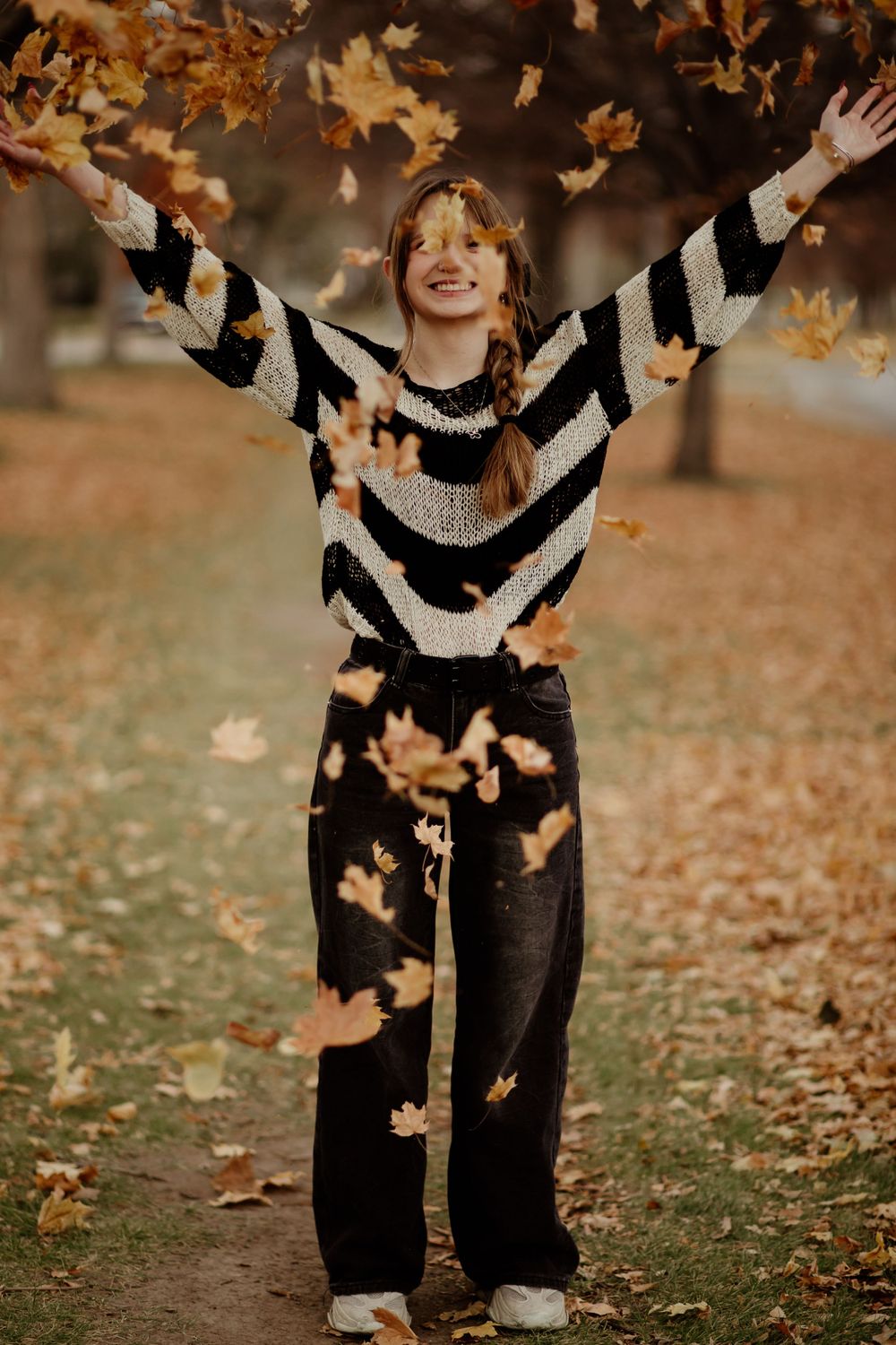 Playful autumn scene with falling leaves and striped sweater in a park setting.