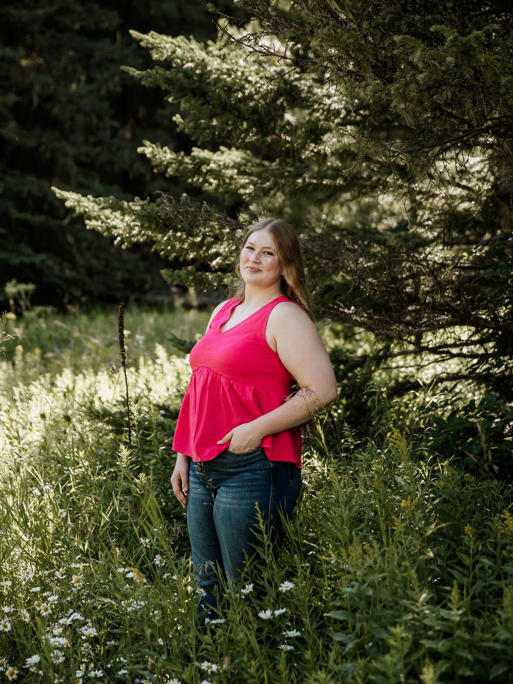 Candid portraits in a sunlit meadow wearing a bright pink top and jeans.