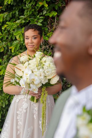 A beautiful wedding scene with a stunning white orchid bouquet against lush green foliage in an outdoor setting.