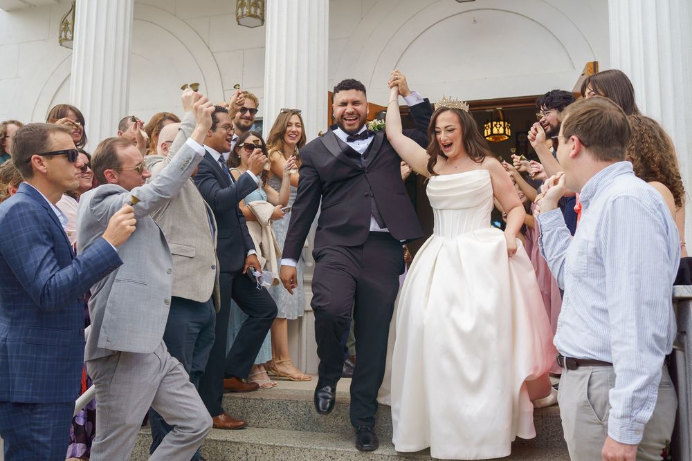 Joyful newlyweds exit church ceremony as guests cheer and celebrate their wedding day outdoors.