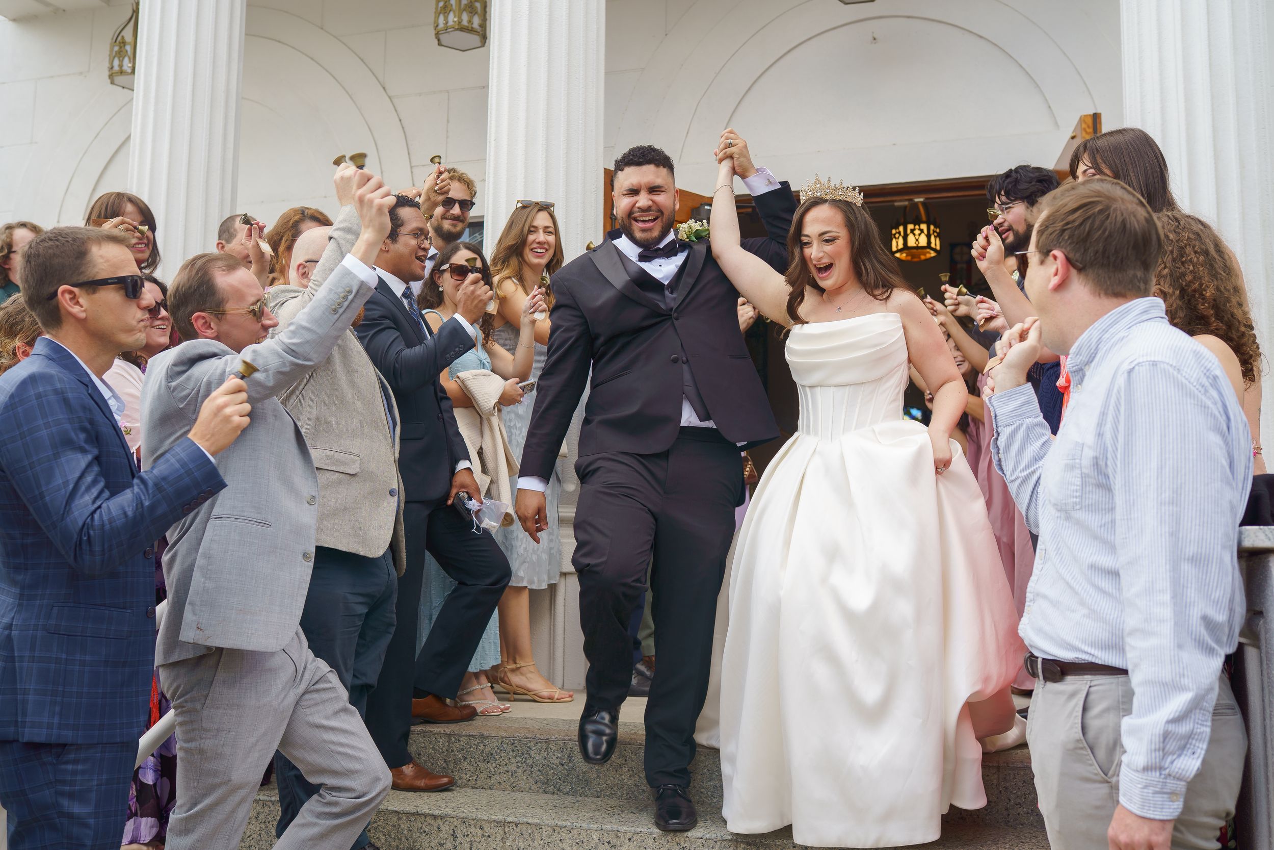 Joyful newlyweds exit church ceremony as guests cheer and celebrate their wedding day outdoors.