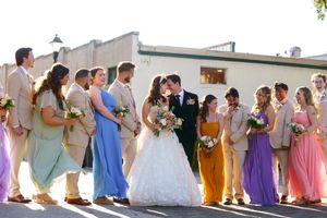 A wedding party poses together outdoors wearing colorful pastel bridesmaid dresses.