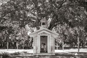 Small white chapel nestled under Spanish moss trees in black and white.