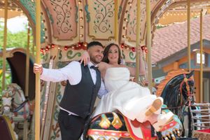 Bride and groom posing on a colorful carousel, celebrating their wedding day at an amusement park.