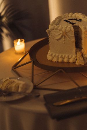 A series of white frosted cake slices arranged on plates with candlelight creating a warm, moody ambiance.