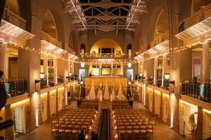 Grand ballroom with rows of chairs and string lights creating an elegant wedding ceremony venue.