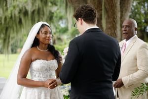 Bride in white lace gown and veil exchanges vows with groom at outdoor wedding ceremony.