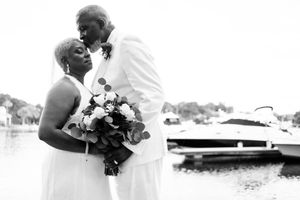 Intimate black and white portrait of couple embracing near waterfront with bouquet.
