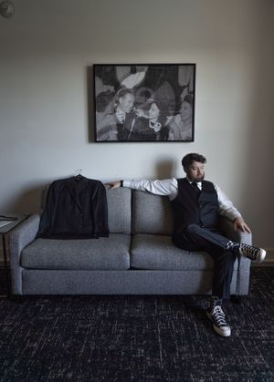 Artistic portrait of someone sitting on a grey couch with black and white artwork in background.