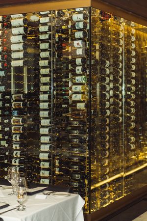 Elegant wine cellar display with backlit bottles arranged in modern rack system beside white tablecloth dining setup.