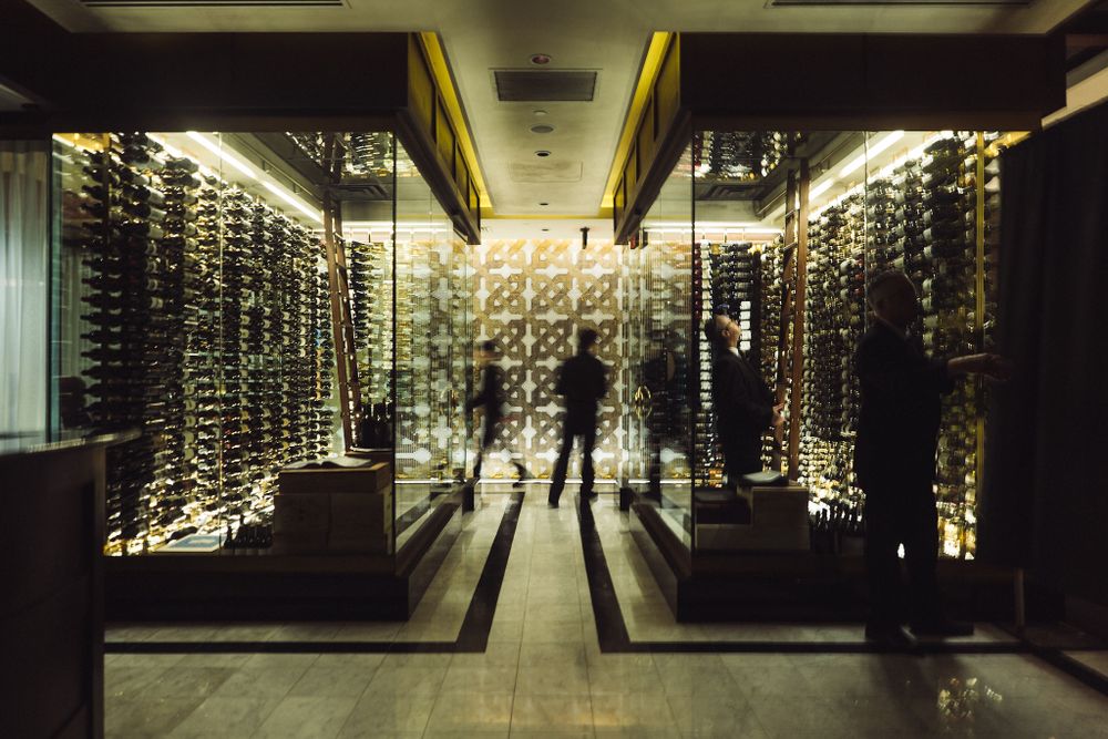 Modern wine cellar with glass walls and dramatic lighting creating reflective silhouettes.